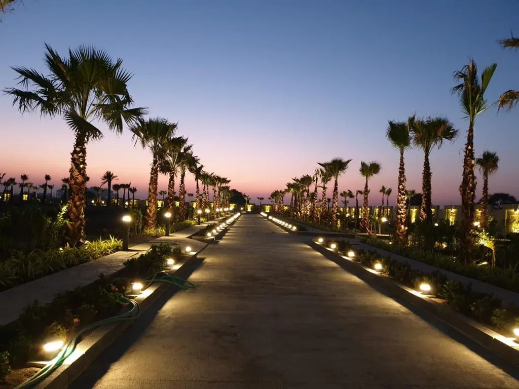 A palm-lined avenue at dusk at The Privé, pathway lights glowing under a violet-rose sky, Indore